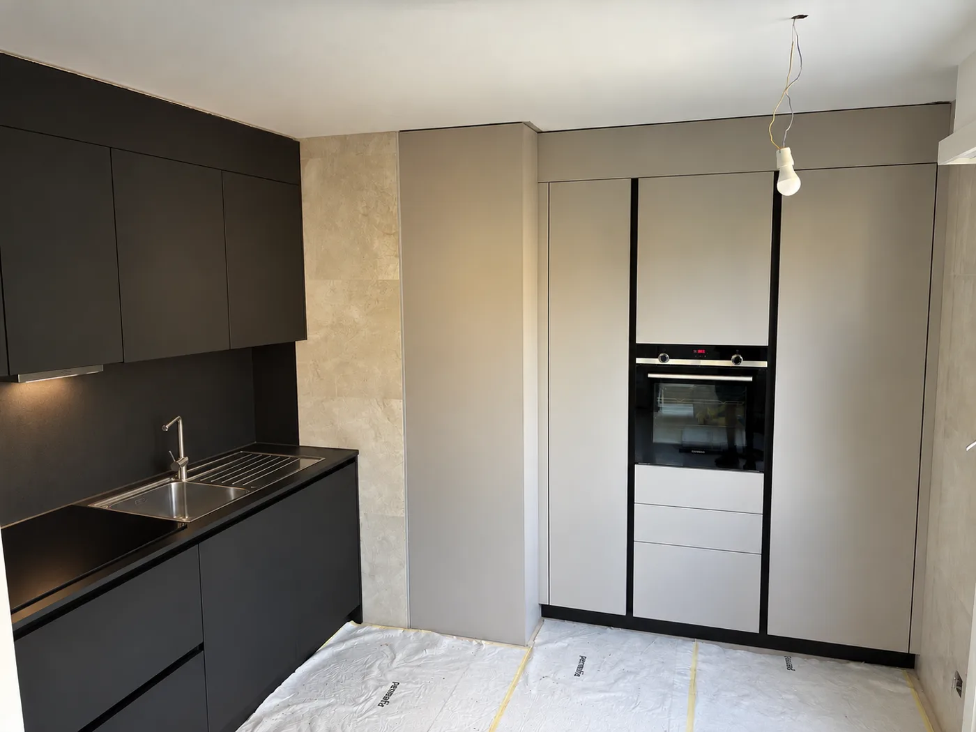 Après : cuisine à façades noires mates, colonnes beiges toute hauteur et éclairage sous meubles